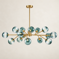 Load image into Gallery viewer, A modern multi-light chandelier with a brushed gold metal frame and translucent smoky blue glass globes, suspended from a matching gold ceiling canopy against a warm off-white background.
