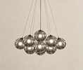 Load image into Gallery viewer, A modern multi-light pendant chandelier with nine reflective smoked glass globes suspended by thin black cords against a warm beige textured wall.
