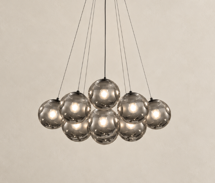 A modern multi-light pendant chandelier with nine reflective smoked glass globes suspended by thin black cords against a warm beige textured wall.
