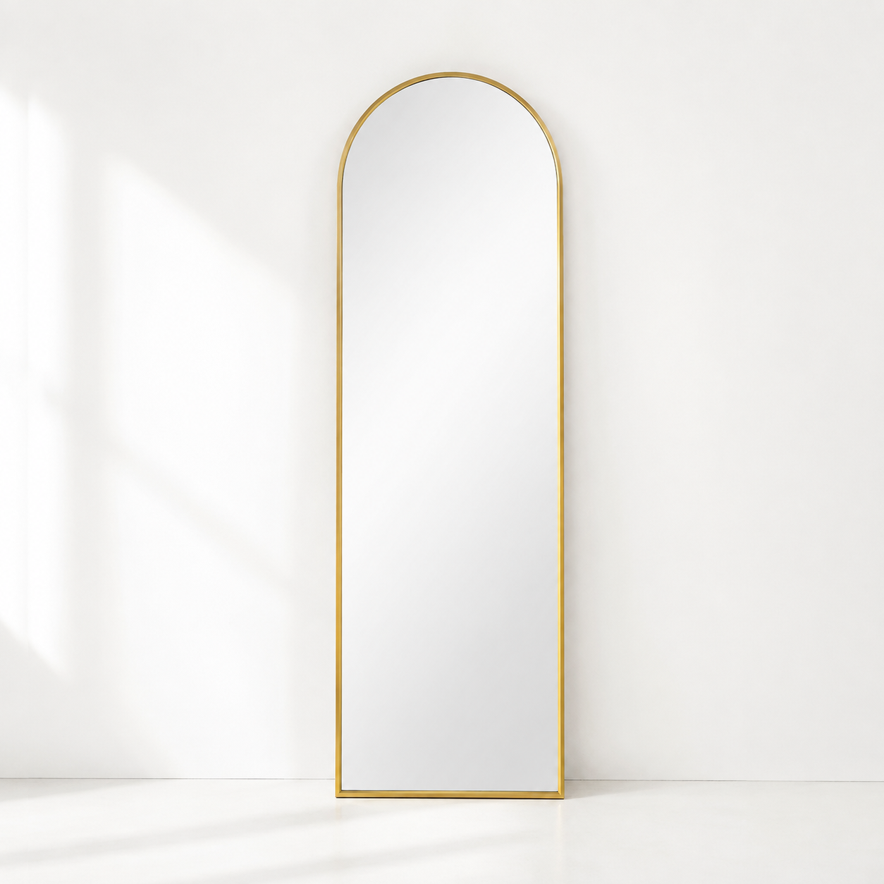 gold arched mirror in an all white room leaning against the wall