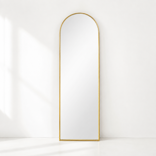 gold arched mirror in an all white room leaning against the wall