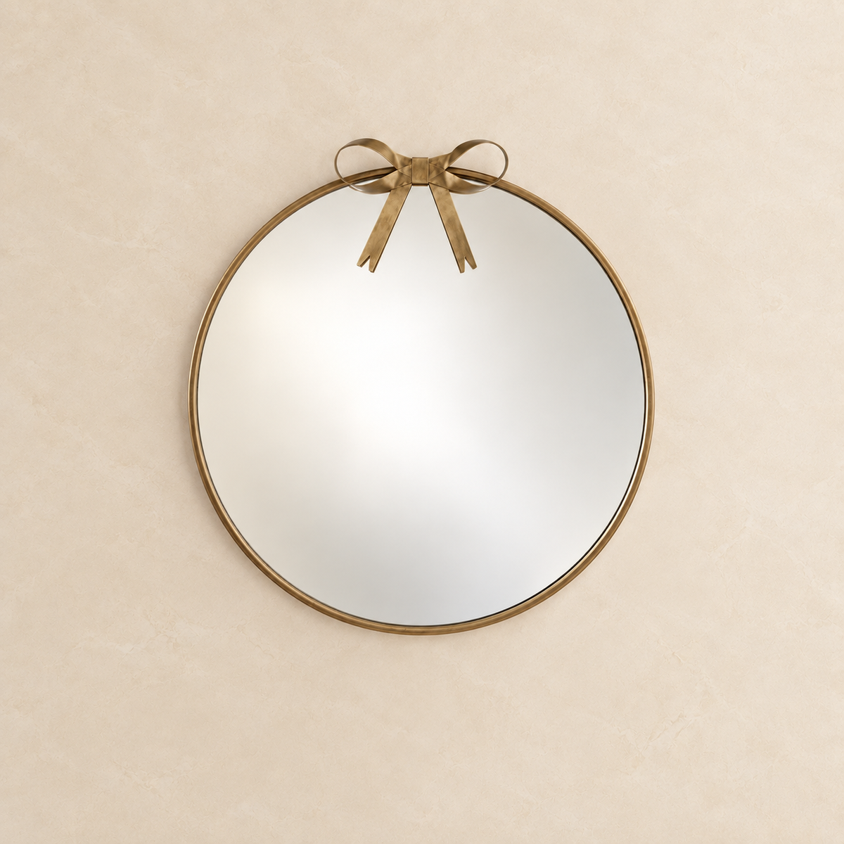 gold roundwall mirror with a distressed brass frame and a matching bow detail at the top, mounted on a textured beige wall