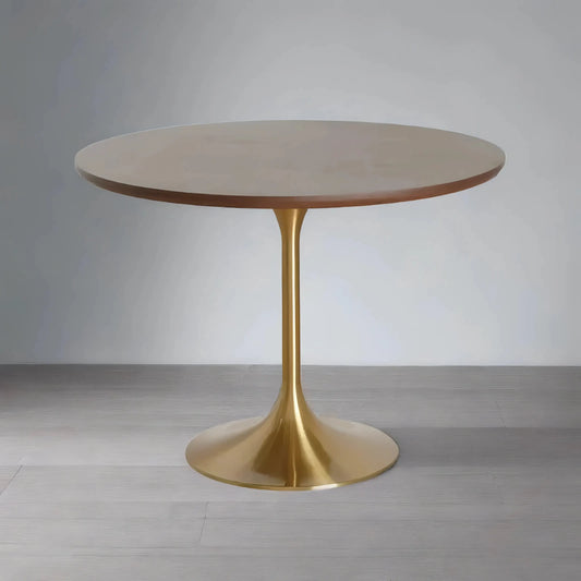 A modern House of Effy round cafe table with a sleek beige top and a shiny gold pedestal base, placed on a wooden floor against a gray wall.