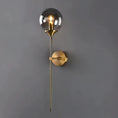 Load image into Gallery viewer, A modern HOUSE OF EFFY wall sconce with a golden base and rod supporting a translucent hand-cut glass spherical shade with an exposed bulb.
