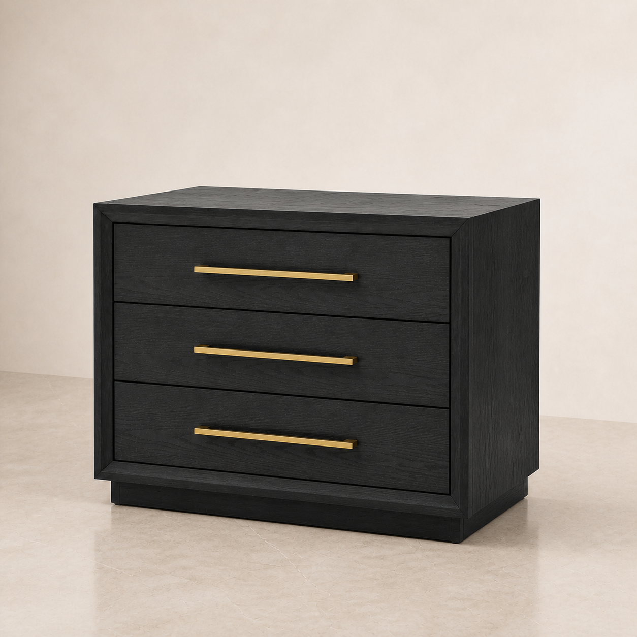 A three-drawer nightstand or side table in black wood with three slim gold metal handles, shown on a light beige studio floor against a matching beige wall.