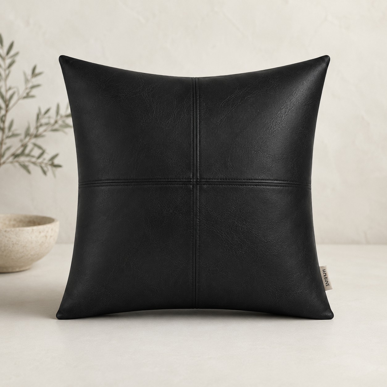leather pillow cover that is black in color next to a bowl and faux plant