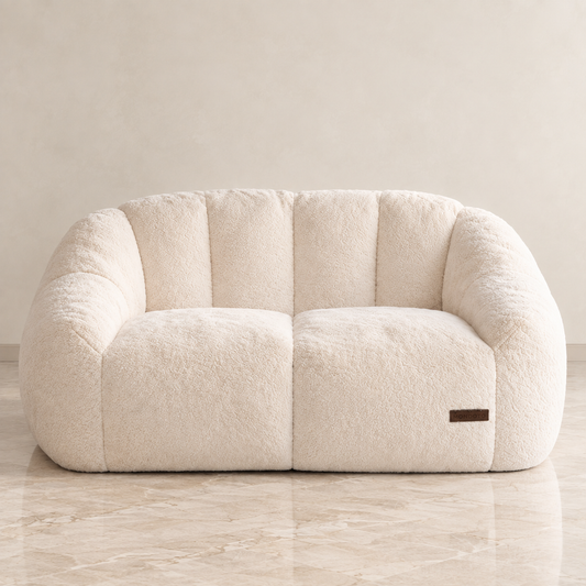 love seat sofa with a rounded, bubble-like silhouette, set against a neutral beige wall and light marble floor.