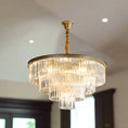 Load image into Gallery viewer, A round, multi-tiered CRYSTAL CHANDELIER by House of Effy with a gold fixture hangs from the ceiling, casting light and adding sophisticated beauty to the room.
