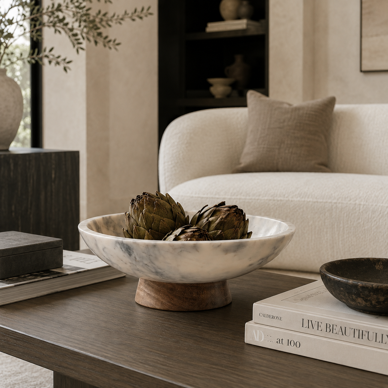 marble bowl with a wooden base holding artichokes, styled on a dark wood coffee table in a modern living room setting.