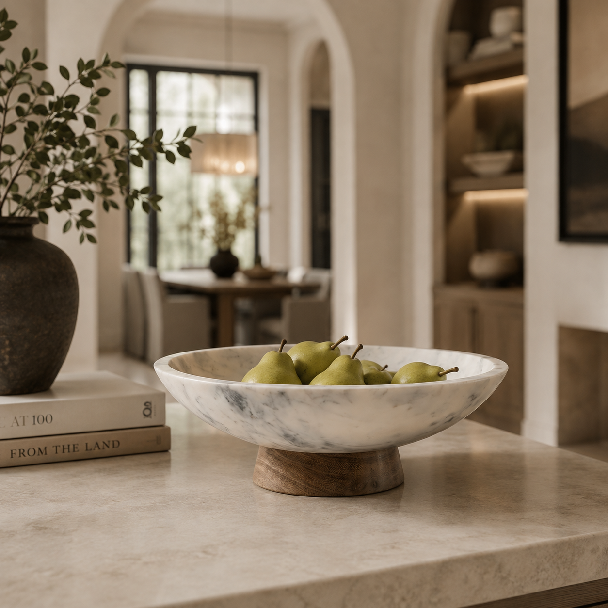 marble bowl with a wooden base, filled with green pears, styled on a marble countertop in a warm, modern kitchen setting.