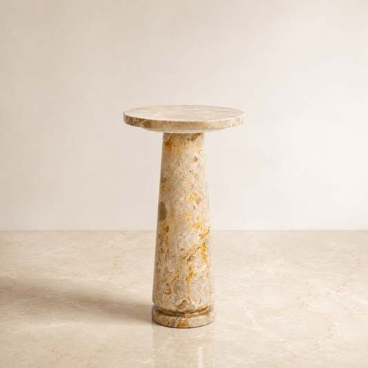 A round marble side table with a flared top and a tapered column base, featuring natural beige and gold veining, set against a neutral beige background.