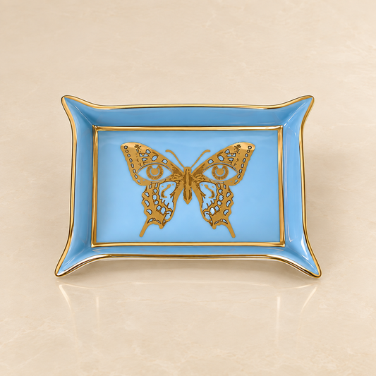 A rectangular light blue ceramic dish with gold trim and a detailed gold butterfly design in the center, set against a warm beige marble background.