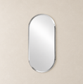 Load image into Gallery viewer, An oval wall mirror with a polished silver frame, centered on a textured beige wall.

