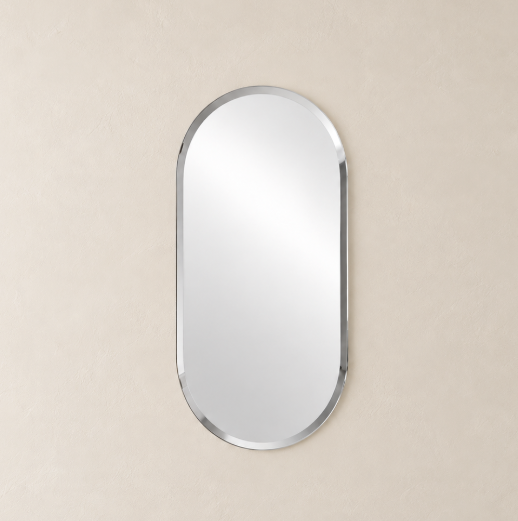 An oval wall mirror with a polished silver frame, centered on a textured beige wall.