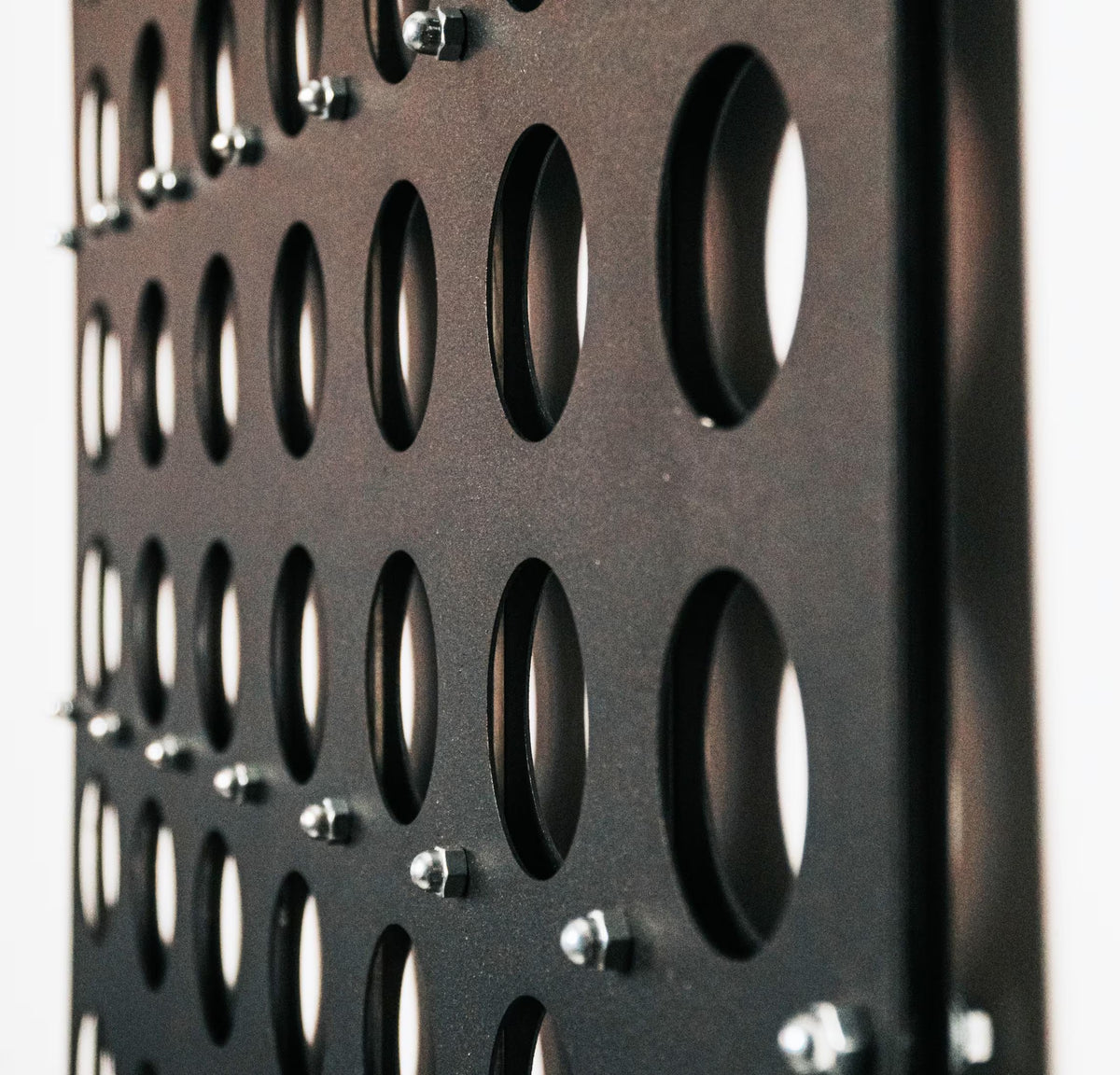 Close-up of black life-size wall mounted Four in a Row game board with metal pegs in circular slots on white background