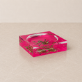 Load image into Gallery viewer, A square acrylic ashtray with a vibrant hot pink background and green floral patterns, featuring a clear glass bowl in the center and the name 'niedlata mayer' printed on the side, set on a beige marble surface.
