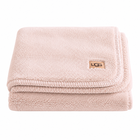 A folded light pink UGG pink throw blanket with a small tan UGG logo patch on the corner, set against a plain white background.
