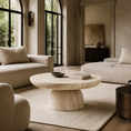 Load image into Gallery viewer, A round stone coffee table in a warm beige marble finish, styled in a luxurious, sunlit living room with cream-colored sofas, a neutral rug, and tall arched windows.
