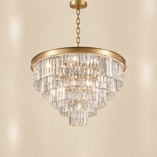 A tiered round gold crystal chandelier with a brushed gold metal frame and chain, hanging against a warm beige wall.