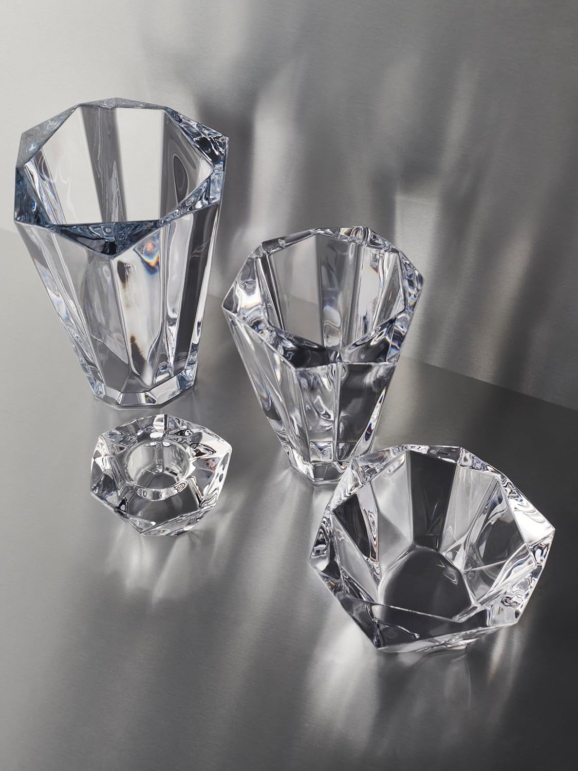Set of clear faceted crystal decorative bowls and vases with geometric shapes on a reflective surface