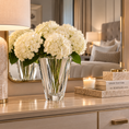 Load image into Gallery viewer, White hydrangea flowers arranged in a shannon crystal vase on a light wood dresser, with a lit lamp, candle, books, and a mirror reflecting a softly styled bedroom.
