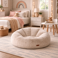 Load image into Gallery viewer, A round, plush beige sofa chair with a soft, cushioned interior sits on a striped rug in a cozy, styled children's bedroom. The room features a bed with pink and beige bedding, a small side table with teddy bears, and warm string lights.

