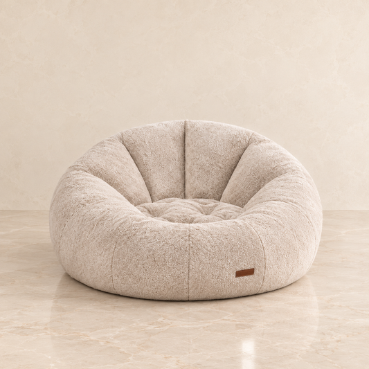 A round, tufted sofa chair in a textured beige fabric, set against a matching beige marble floor and wall background.