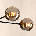 Load image into Gallery viewer, A close-up of a modern two-light sputnik chandelier with spherical smoked glass shades and visible warm Edison bulbs on black metal arms, set against a plain light beige background.
