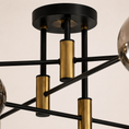 Load image into Gallery viewer, Modern geometric chandelier with a black metal frame, brushed gold cylindrical accents, and partial smoked glass globes, shown against a warm off-white background.

