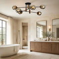 Load image into Gallery viewer, Sputnik chandelier fixture with six spherical glass shades and warm metallic accents, installed in a bright contemporary bathroom with a freestanding tub, wood vanity, and large mirrors.
