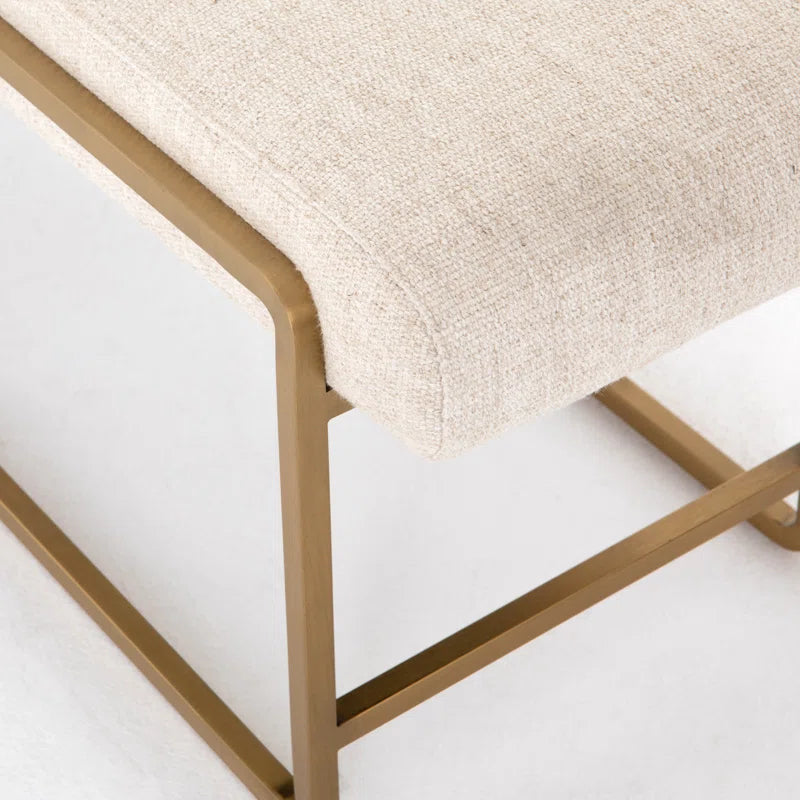 Close-up of beige upholstered bench seat with brass-finished steel frame featuring dramatic bullnose edging