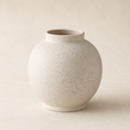 Load image into Gallery viewer, A small round white ceramic vase with a textured, speckled off-white finish and a short flared rim, set against a neutral beige background.
