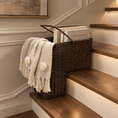 Load image into Gallery viewer, a wicker basket for stairs with handles sits on a wooden staircase landing, holding books and draped with a cream knit throw blanket featuring pom-poms and fringe.

