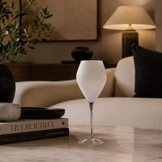 wine glasses with a clear stem and base, styled on a marble table in a cozy, warmly lit living room setting.
