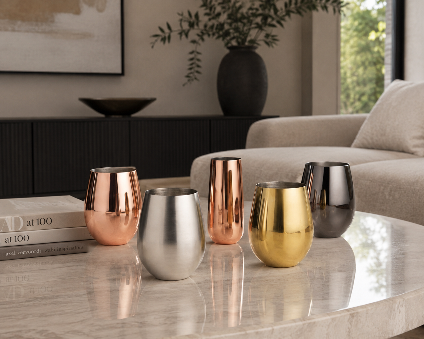 Wine glasses in silver, gold, and black, arranged on a marble coffee table in a modern living room setting.