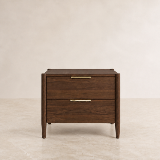 A mid-century modern two-drawer nightstand in dark brown wood with slim brass handles, set against a neutral beige background.
